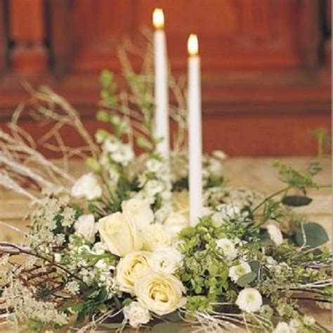 A White And Green Floral Centerpiece With Tall And Thin Candles Is A