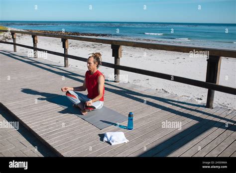 Man Meditating While Practicing Yoga On Floorboard At Beach During