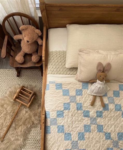 A Teddy Bear Sitting On Top Of A Bed Next To A Rocking Chair And Blanket