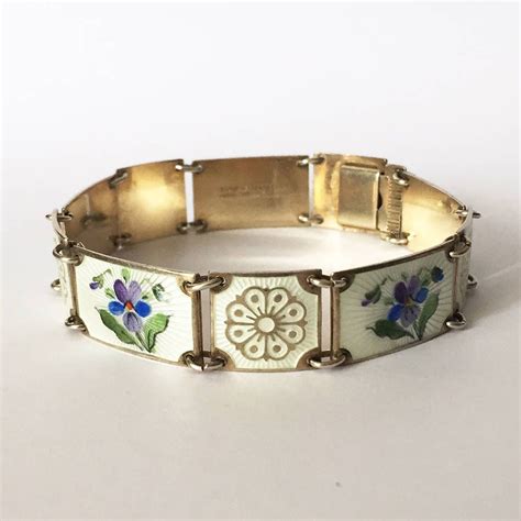 A Close Up Of A Bracelet On A White Surface With Blue Flowers And Green