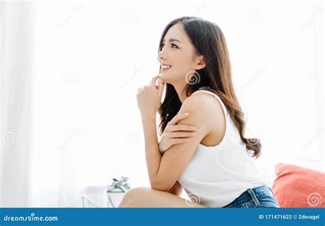 Side View Of Smiling Beautiful Asian Woman Sitting In Her Bed And Looks