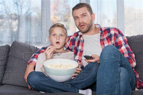 Scared Father And Son Eating Popcorn And Watching Tv Together Stock