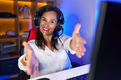 Middle Age Brunette Woman Playing Video Games Looking At The Camera Smiling With Open Arms For