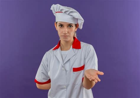 Joven bonita cocinera en uniforme de chef mostrando la mano vacía