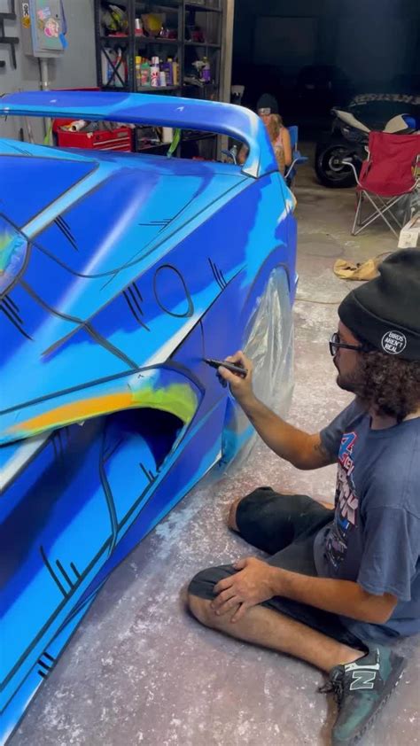 A Man Is Painting The Side Of A Blue Car With Graffiti On It S Sides