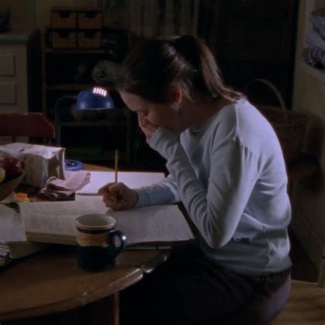 A Woman Sitting At A Table Writing On A Piece Of Paper With A Pen In