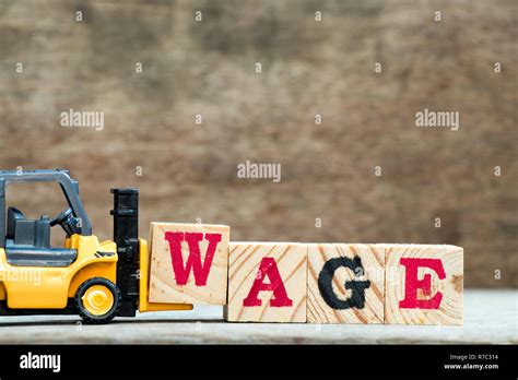 Yellow Toy Forklift Hold Letter Block W To Complete Word Wage On Wood