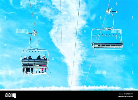 Two Chairs Of A Ski Lift Against A Clear Blue Sky One Chair Has Skiers