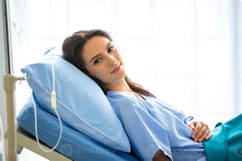 Portrait Of Young Female Patient Lying On Clinic Bed Wearing Hospital