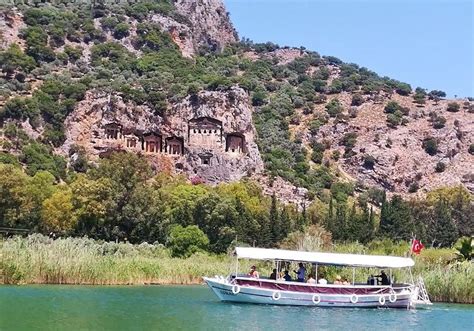 A Boat Is On The Water In Front Of A Mountain With Caves And Trees