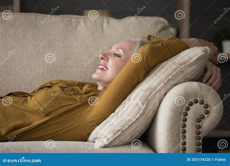 Happy Cheerful Mature Woman Lying On Comfortable Couch Stock Photo