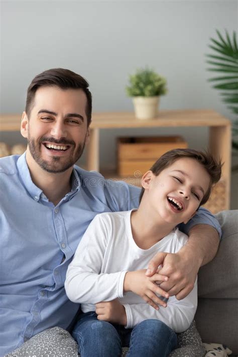 Pai Abraçando A Família Do Filho Sentado No Sofá Olhando A Câmera Foto