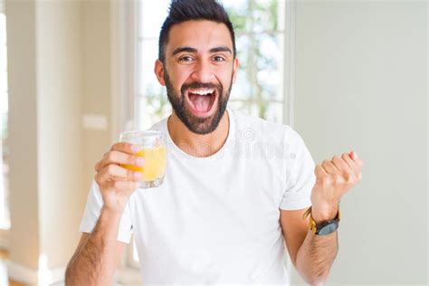 Handsome Hispanic Man Drinking Healthy Orange Juice Screaming Proud And