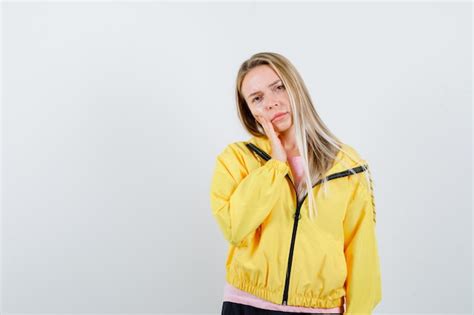 Fille blonde en veste jaune tenant la main sur la joue et à la grave Photo Gratuite