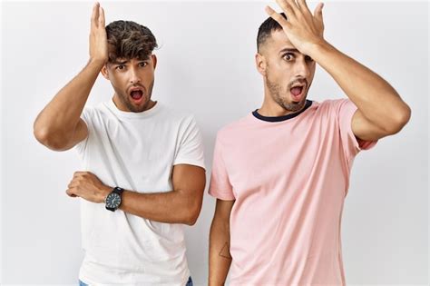 Jeune Couple Gay Debout Sur Fond Isolé Surpris Avec La Main Sur La Tête Pour Erreur Rappelez