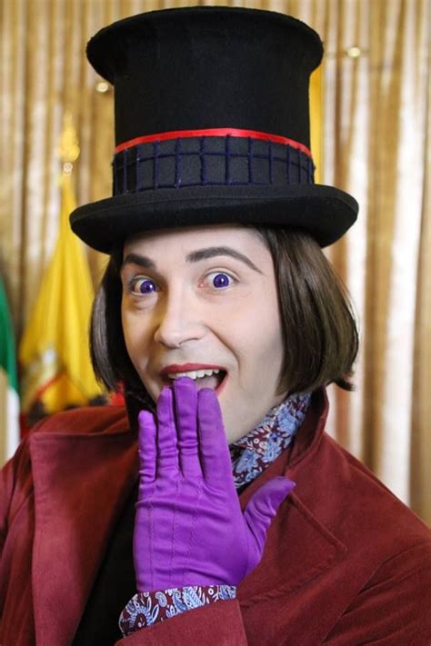 A Man Wearing A Top Hat And Purple Gloves With His Hands On His Face While Smiling At The Camera