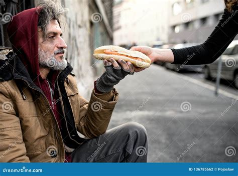 Unrecognizable Woman Giving Food To Homeless Beggar Man Sitting In City