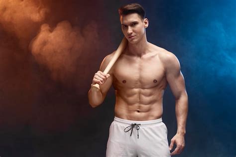 Culturista de hombre fuerte y en forma con bate de béisbol posando con