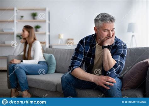 Offended Mature Man And Woman Sitting On Different Sides Of Sofa After