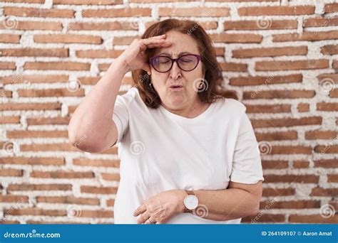 Senior Woman With Glasses Standing Over Bricks Wall Worried And Stressed About A Problem With