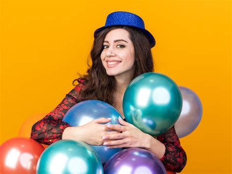 Sonriente joven fiestera vistiendo gorro de fiesta de pie detrás de