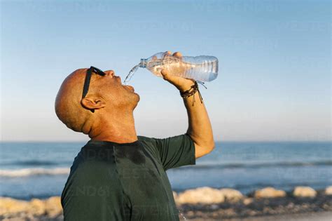 Senior Man Drinking Water While Standing Against Clear Sky Stock Photo