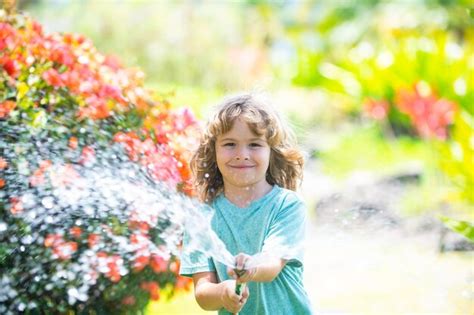 Un niño adorable regando las plantas con un rociador de manguera con