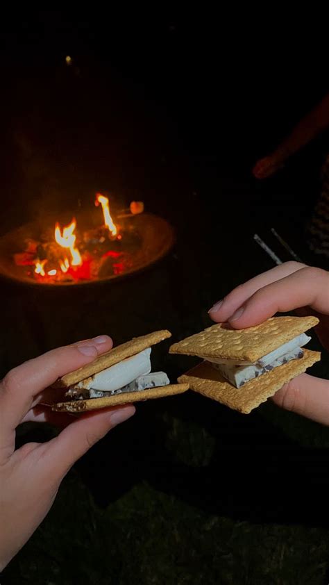 Two People Holding Sandwiches In Front Of An Open Fire Pit At Night