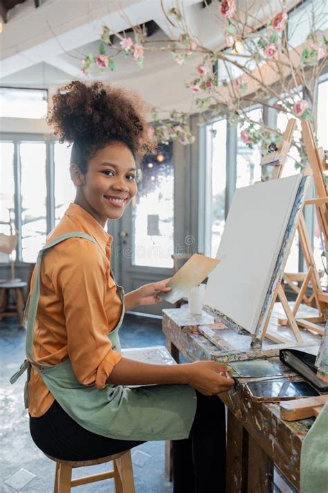 African American Mature Female Artist Smiling At Camera While Painting