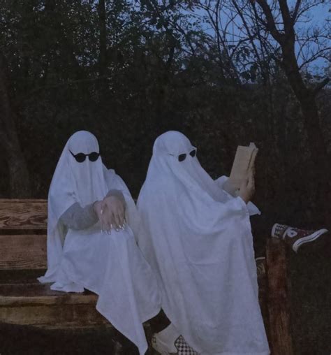 Two People In White Ghost Costumes Sitting On A Bench With Their Feet