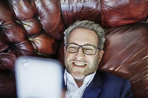 Smiling Mature Businessman Lying Down Looking On Cell Phone Stock Photo