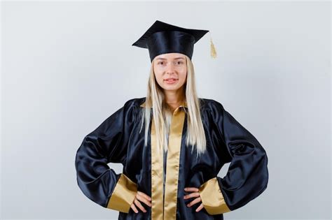 Fille Blonde En Robe De Graduation Et Casquette Tenant Les Mains Sur La Taille Et L Air Confiant