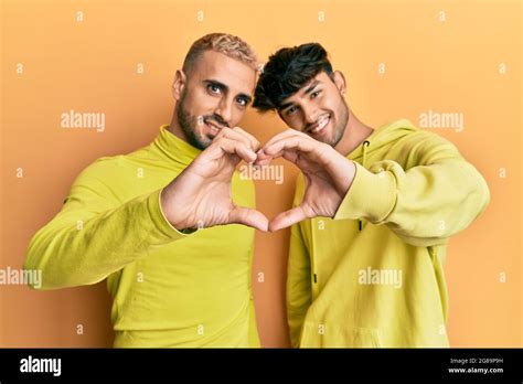 Homosexual Gay Couple Standing Together Wearing Yellow Clothes Smiling In Love Doing Heart