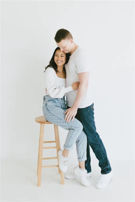 Couple Poses While Girl Sits On A Stool And Guy Hugs Her From The Side Photography Outfits