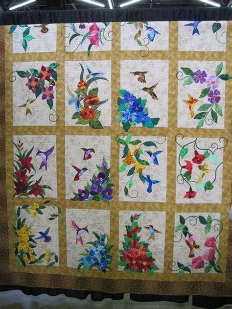 A Quilt Made With Flowers And Birds On The Front Is Hanging From A