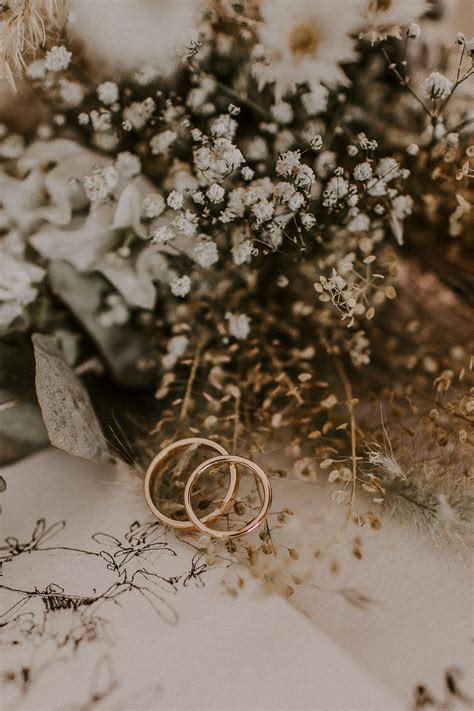 Two Gold Wedding Rings Sitting On Top Of A Table Next To Flowers And