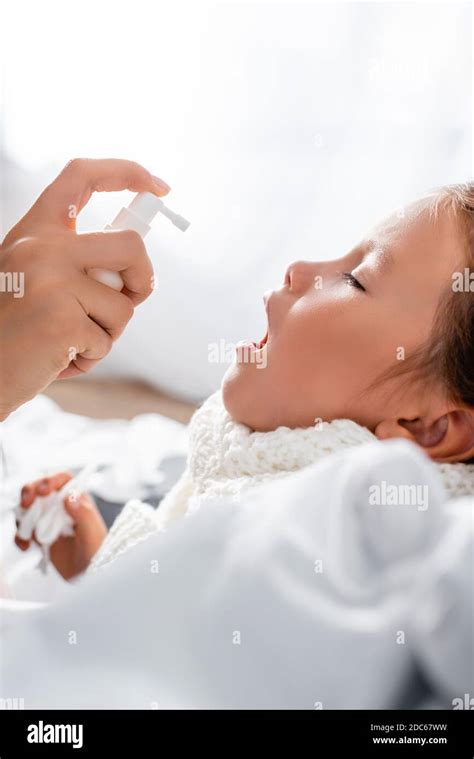 Side View Of Mother Applying Spray On Sore Throat Of Diseased Daughter