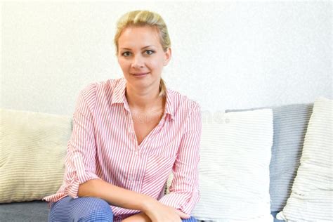Beautiful Blonde Woman Sitting On A Sofa In An Apartment Looking At Camera Stock Photo Image