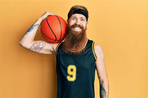 Redhead Man With Long Beard Wearing Basketball Uniform Holding Ball