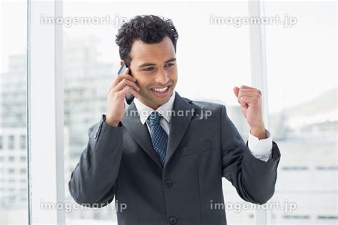 Happy Elegant Young Businessman Using Cellphone In A Bright Officeの写真素材