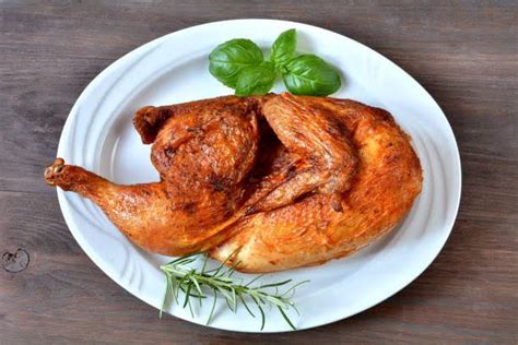 A Whole Chicken On A White Plate With Fresh Herbs