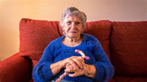 Grandma Holding A Walking Stick While She Sitting On The Sofa At Living