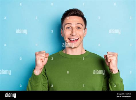 Photo Of Crazy Excited Guy Raise Fists Celebrate Lucky Victory Wear Green Sweater Isolated Blue