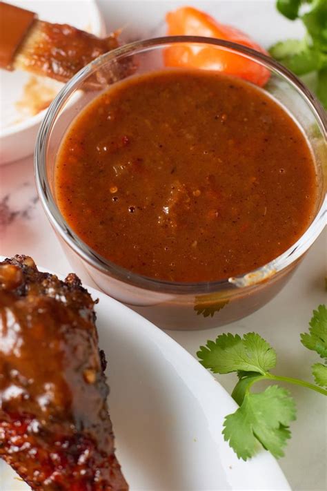 A Bowl Of Jerk Bbq Sauce Next To Cooked Chicken And Fresh Herbs