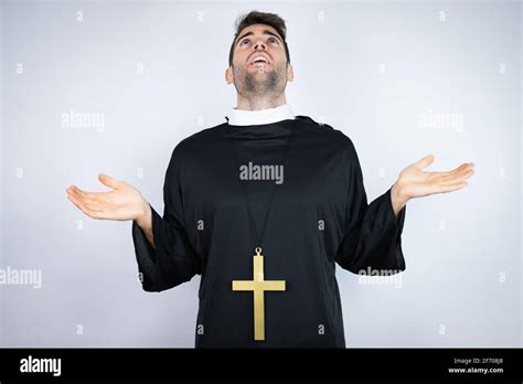 Young Hispanic Man Wearing Priest Uniform Standing Over White