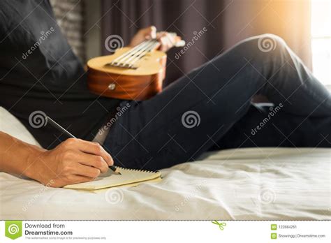 Happy Young Asian Man Playing Ukulele Sitting On Bed In Bedroom Stock