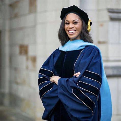 A Woman Wearing A Blue Graduation Gown And Black Cap With Gold Tassel