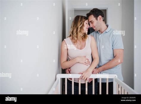 Romantic Couple With Face To Face Standing By Crib At Home Stock Photo