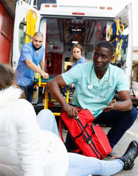 Paramedics Providing First Aid To Injured Woman Near Ambulance Car