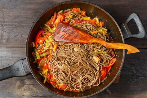 Soba with Vegetables in Soy Sauce with Spices in a Frying Pan with a Wooden Spatula on the Table ...